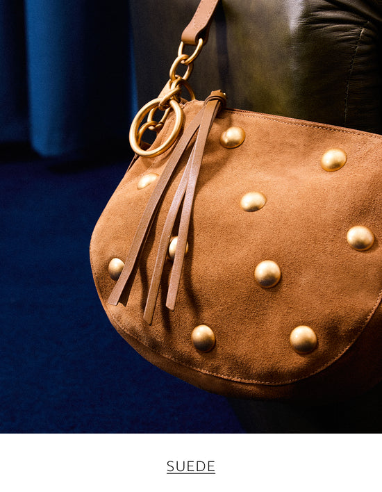 A close-up of a studded, brown suede handbag with fringe-like leather tassels and a gold chain handle. The text 