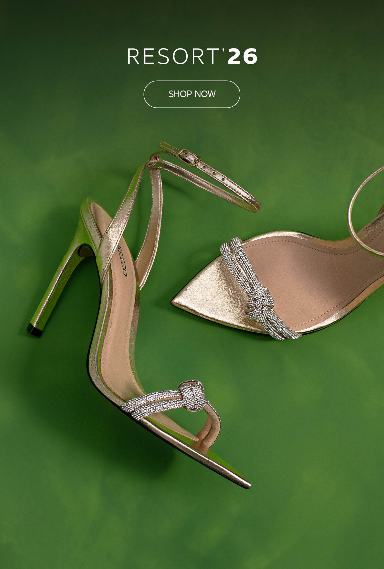 Metallic gold high-heel sandals with crystal-embellished straps displayed on a vibrant green background, promoting the Resort ’26 collection.