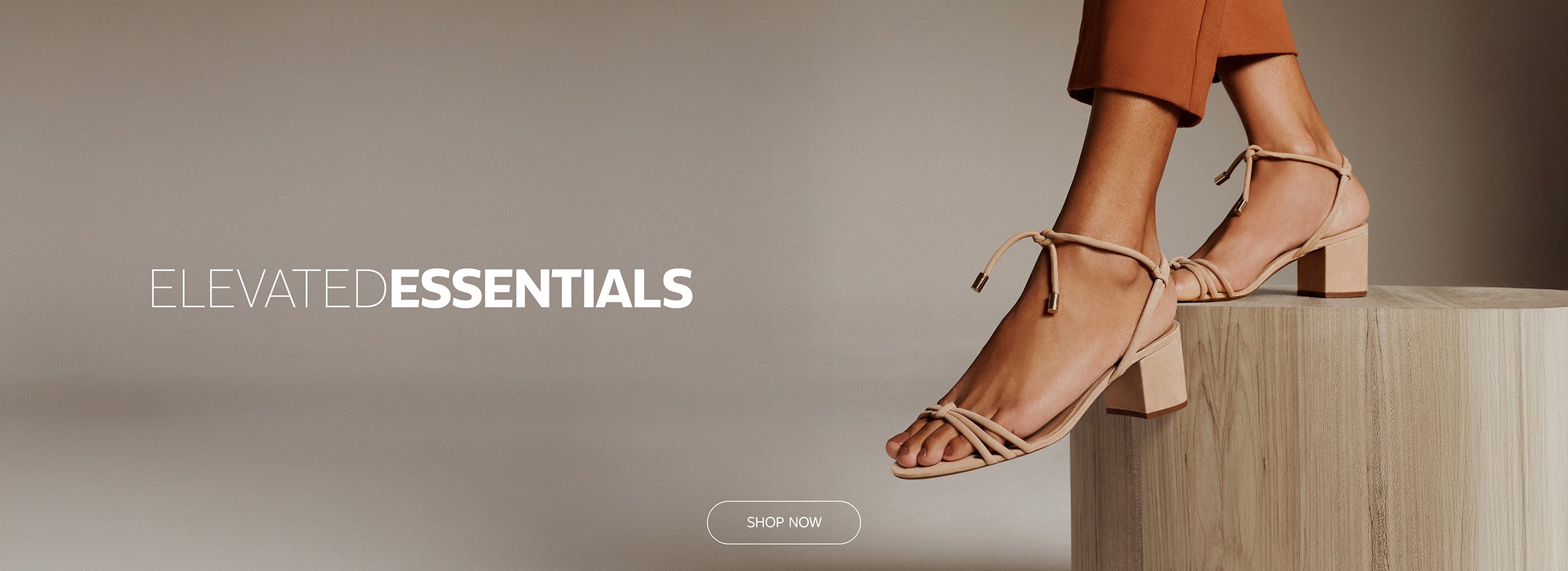 Woman wearing nude block-heeled sandals with minimalist knotted straps, standing on a wooden platform.