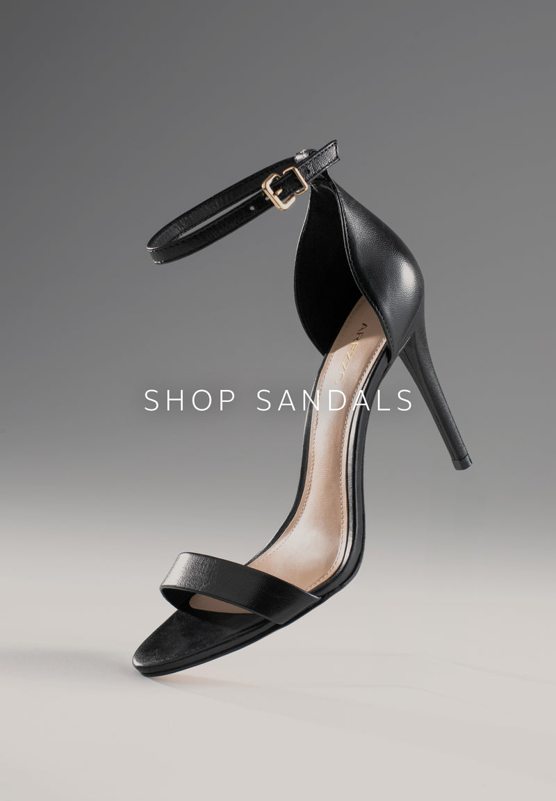 Gold cracked leather sandal. The style features a flat heel and a rounded toe. It has a toe-divider strap connected to a thin strap, both adorned with round pieces linked by a larger central round embellishment. A thin strap runs along the sides, crosses the heel, wraps around the ankle, and fastens with a side buckle. With a beige insole and the brand name engraved on it. 