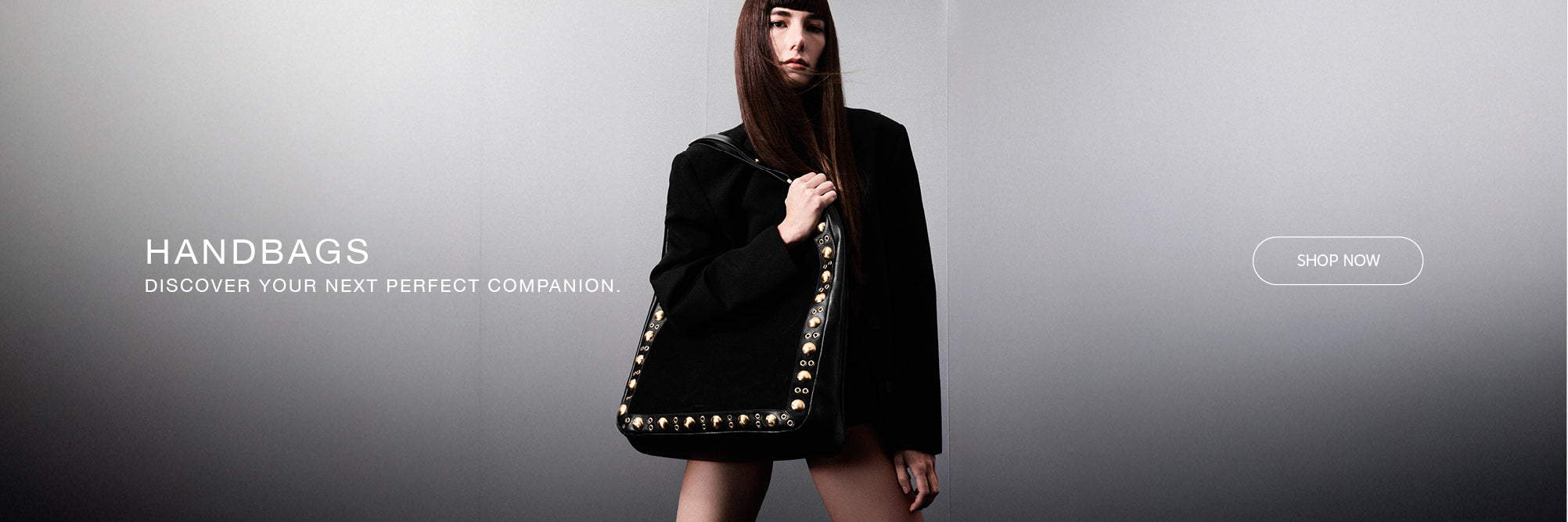Model in black blazer holding a black studded leather shoulder bag. Discover Handbags.