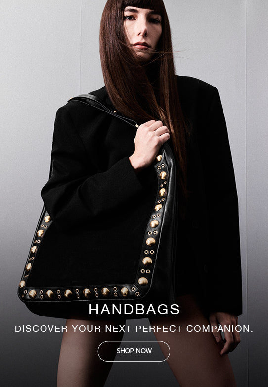 Model in black blazer holding a black studded leather shoulder bag. Discover Handbags.