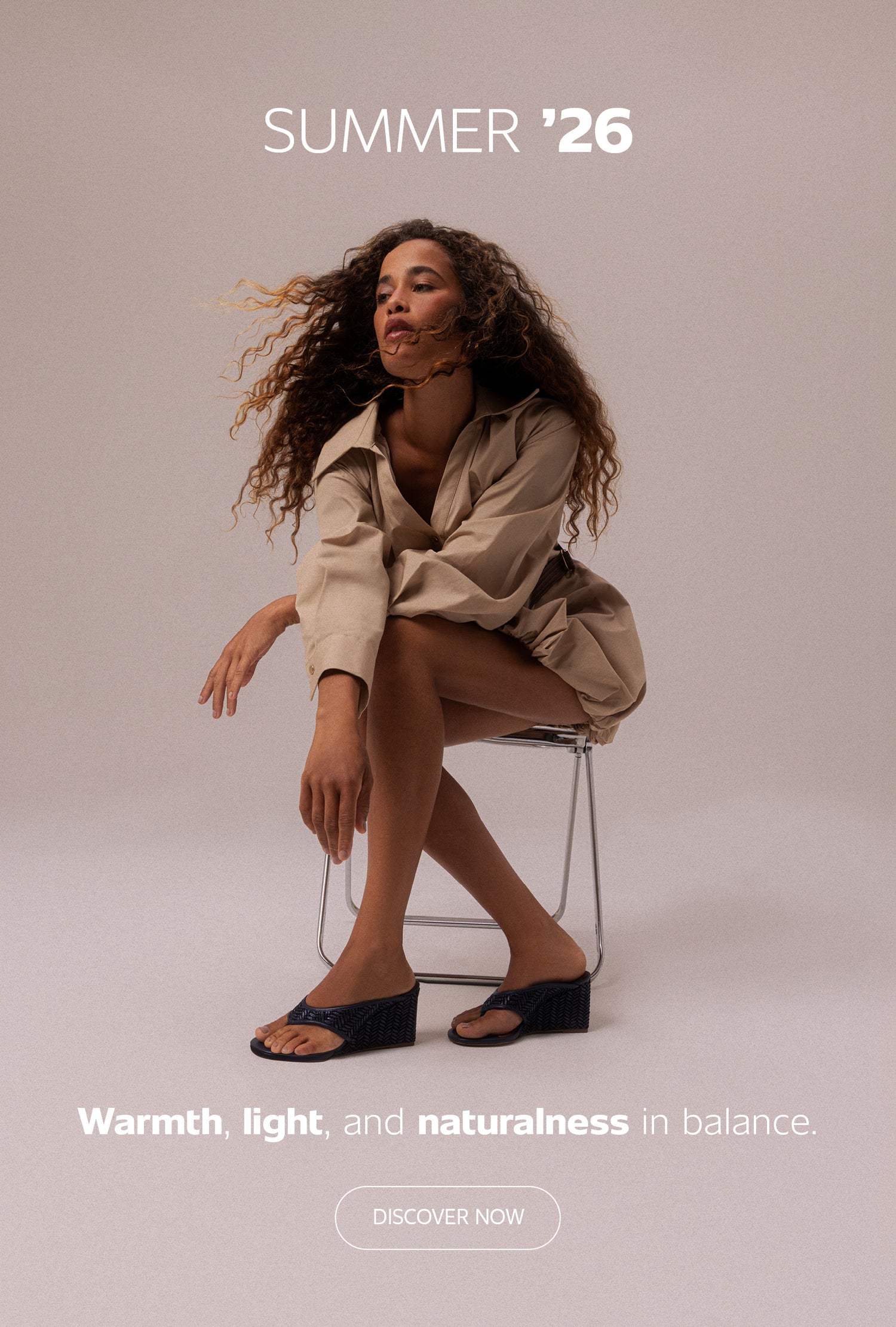 Split banner showing a woman seated on a chair wearing black wedge sandals and a beige outfit on both sides, with centered text “Summer ’26 – Warmth, light, and naturalness in balance” and a “Discover Now” button.