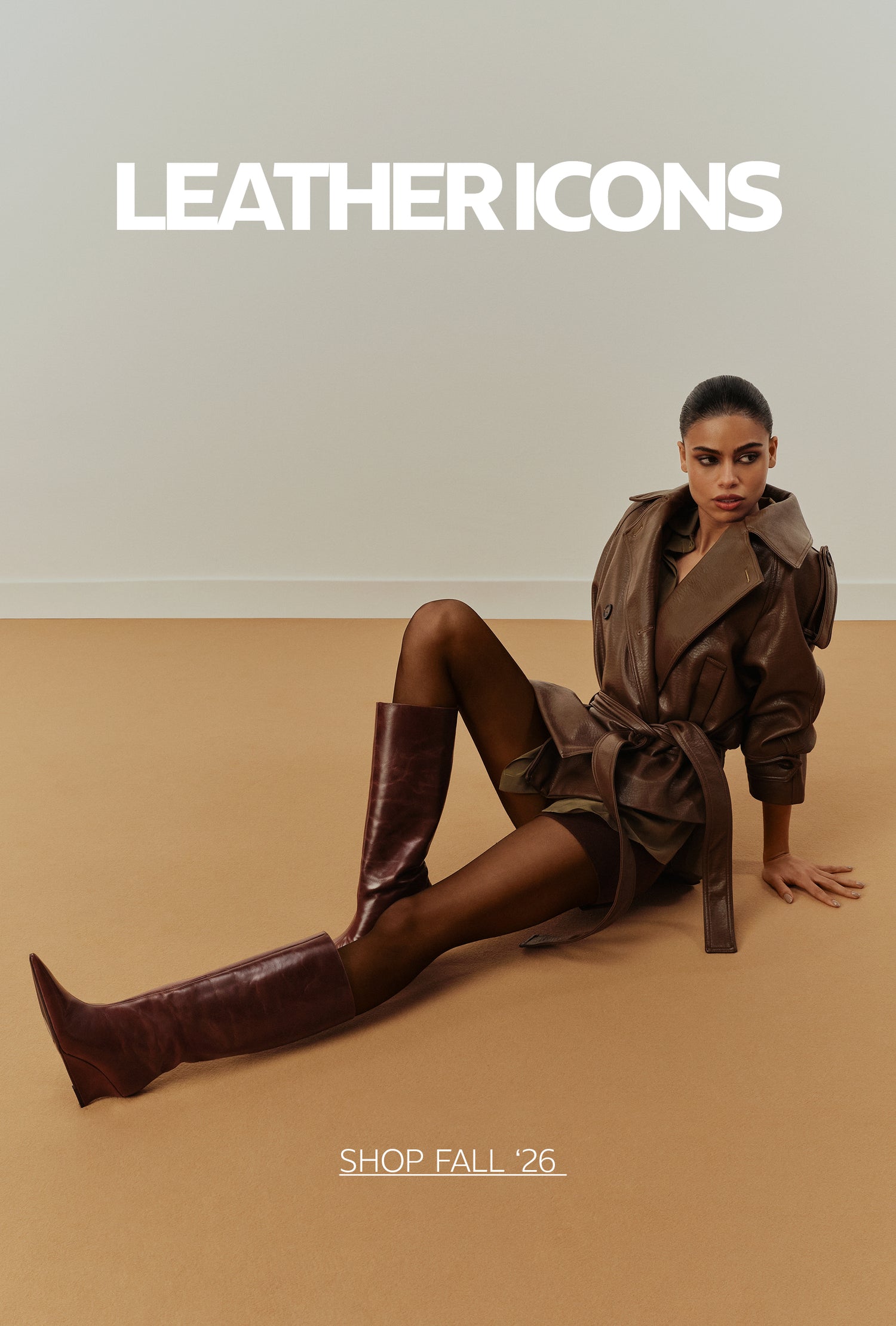 Woman wearing a brown leather jacket and knee-high leather boots, seated on a neutral-toned floor, with “Leather Icons” and “Shop Fall ’26” text.