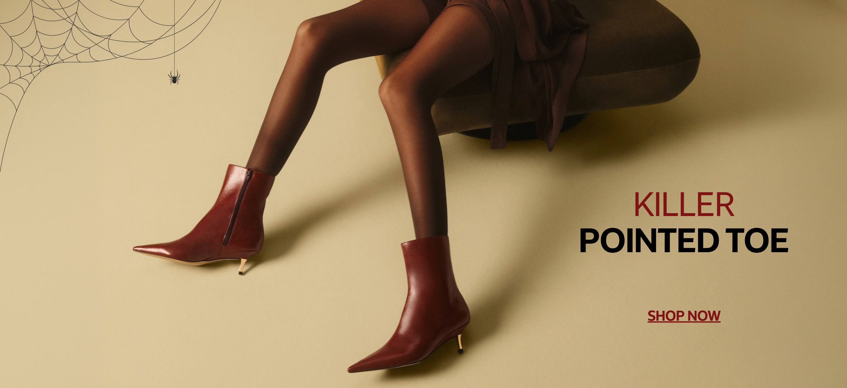 Model wearing burgundy pointed-toe ankle boots with slim heels, seated in a brown armchair against a beige background with a spiderweb graphic. Text reads “Killer Pointed Toe” and “Shop Now.”