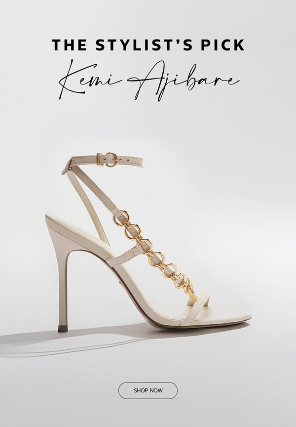Elegant high-heeled sandal in off-white with gold chain-link detailing along the T-strap and ankle buckle, showcased as part of "The Stylist’s Pick" by Kemi Ajibare.