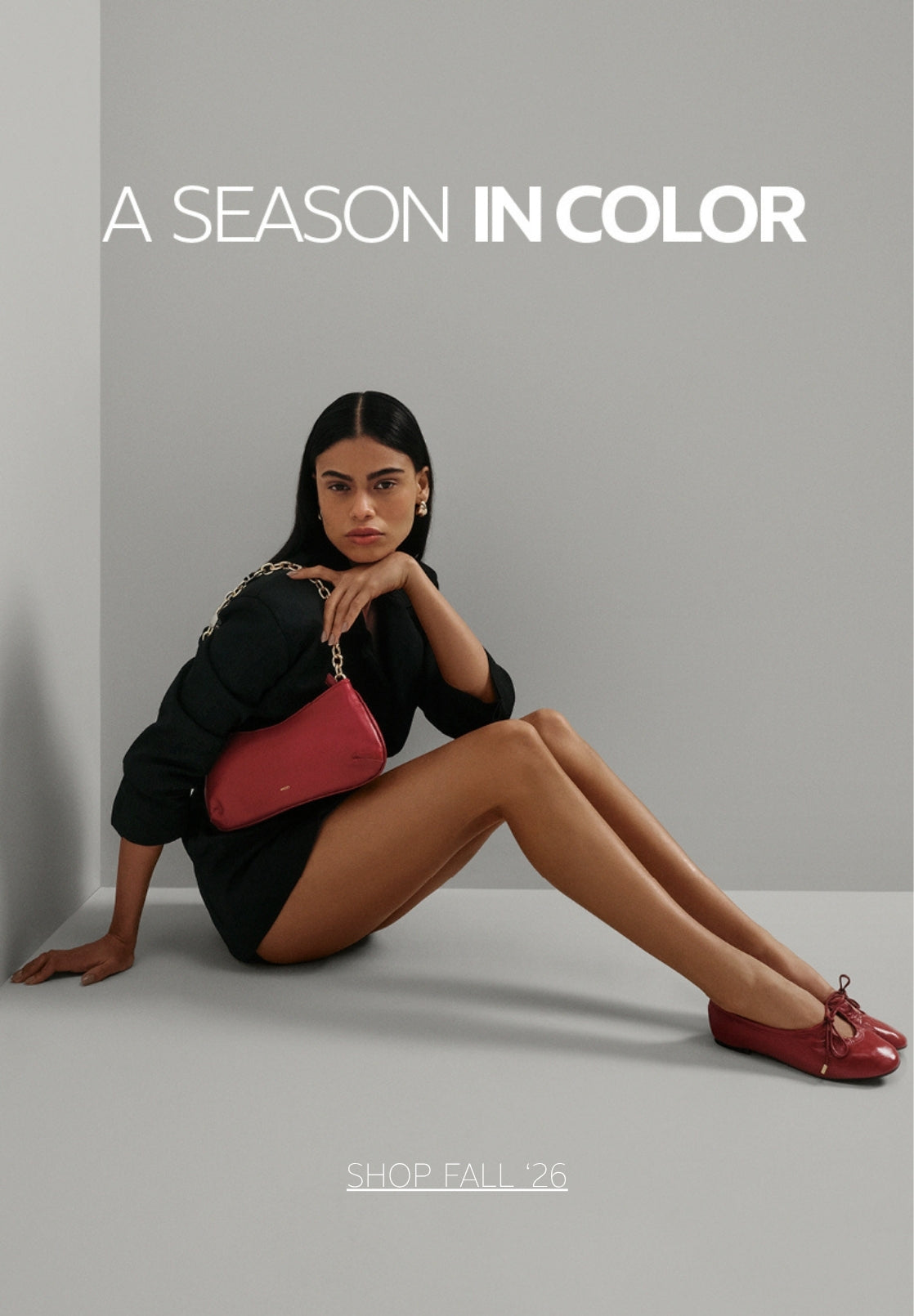 Arezzo Fall ’26 campaign image featuring a woman in a black outfit seated against a gray backdrop, carrying a red handbag and wearing matching red ballet flats. Text reads “A Season in Color” and “Shop Fall ’26.”