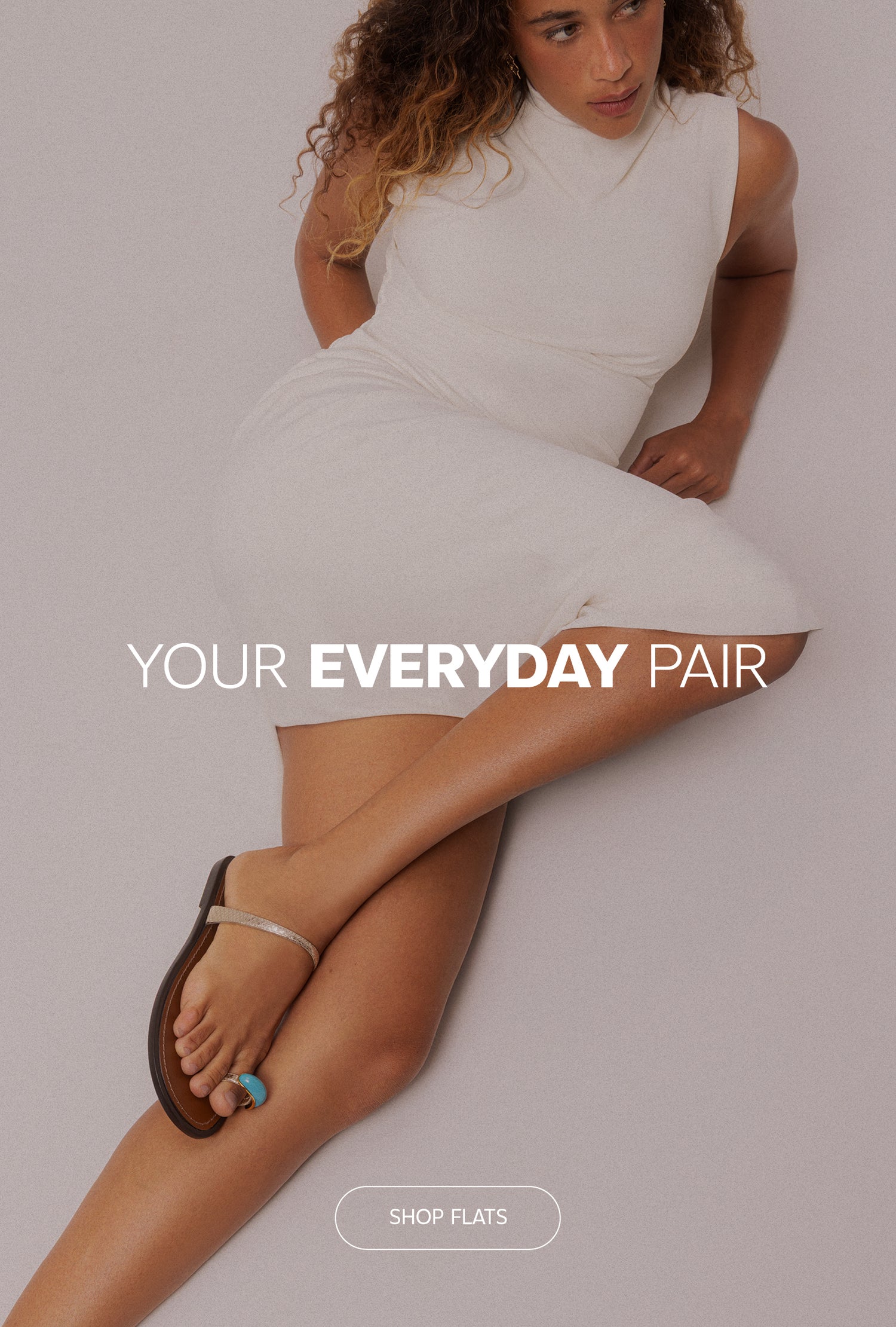 Woman wearing a white dress while reclining on a light neutral surface, featuring metallic thong flat sandals with a turquoise toe ring detail. Overlay text reads "Your Everyday Pair" with a "Shop Flats" button.