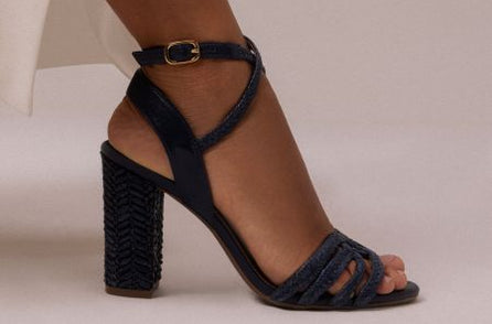 Navy braided high-heel sandal with ankle strap worn by model against a neutral background.